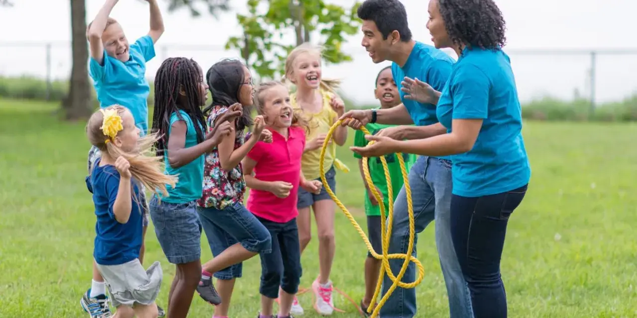 Des enfants et des animateurs jouent à la corde à sauter dans un parc.