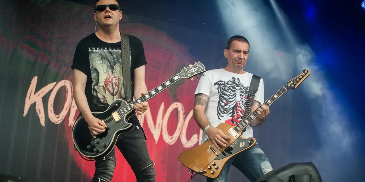 Dwóch gitarzystów na scenie, jeden w czarnej koszulce z sercem, drugi w białej z żebrami. Kocham cię jak Irlandię, grają rocka.