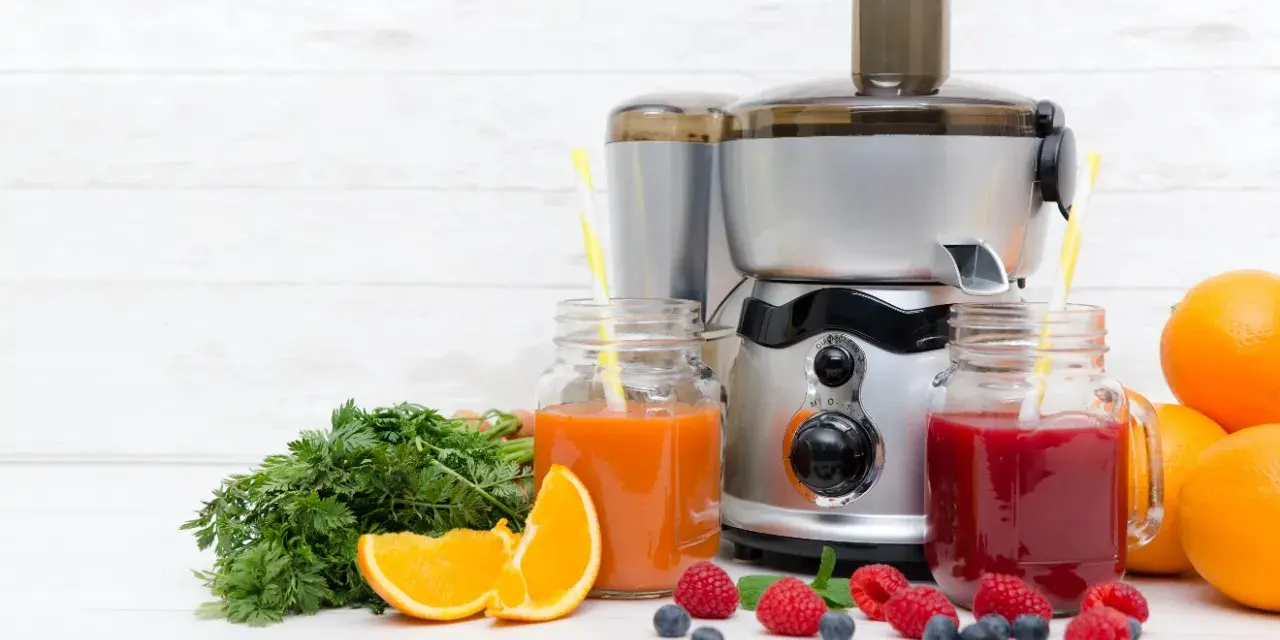 Une centrifugeuse ou extracteur prépare des jus frais avec des fruits et légumes. Ici, des jus d'orange, de carotte et de baies, avec des oranges, des carottes et des baies.