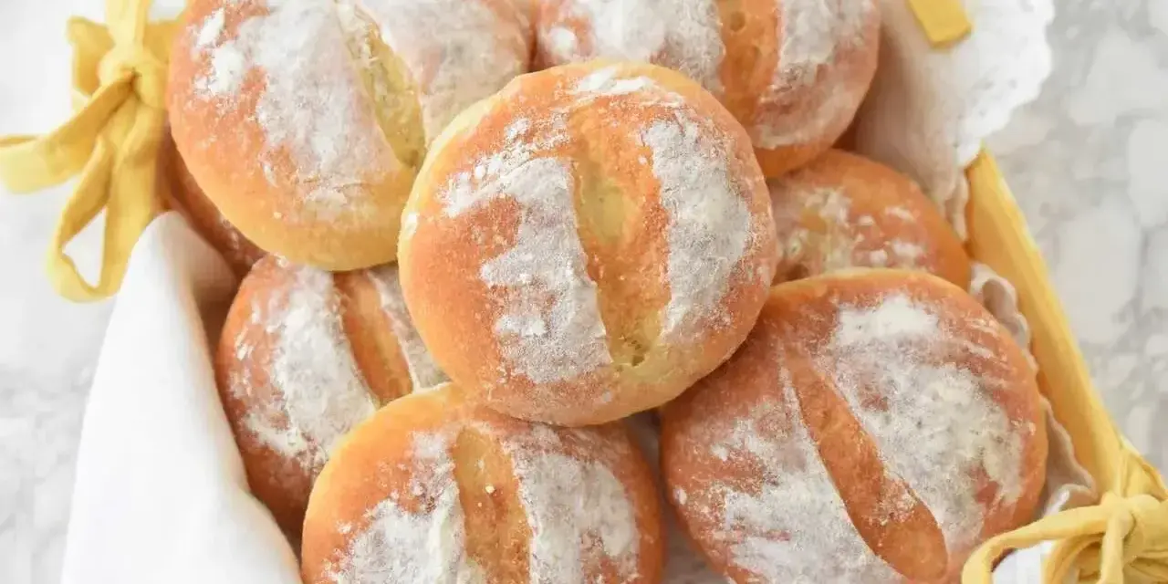 Koszyk z apetycznymi bułkami ziemniaczanymi, posypanymi mąką, ozdobiony żółtą wstążką.