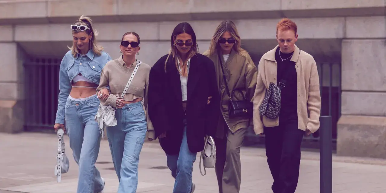 Fünf Freunde spazieren lässig, alle tragen Jeans. Welche Jeans sind in? Weite Schnitte und helle Waschungen dominieren den Look.