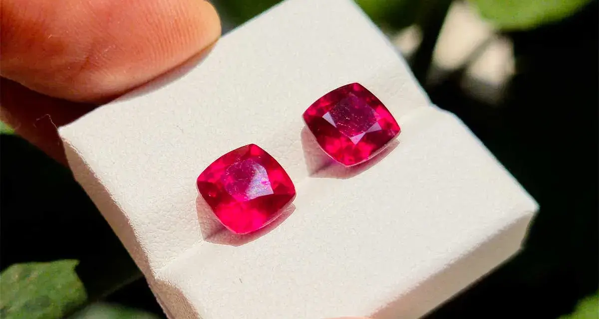 Due gemme rosse intense, la pietra di luglio per eccellenza, brillano su un supporto bianco.