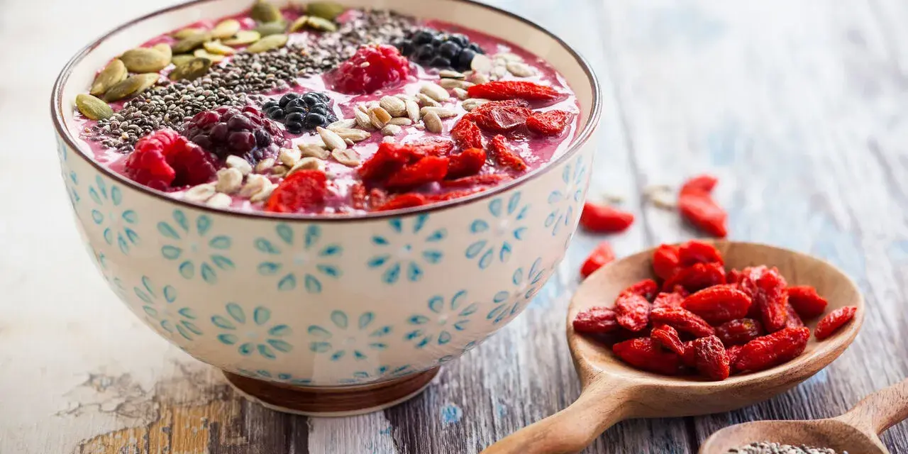 Miseczka smoothie z owocami, nasionami chia, pestkami dyni i słonecznika. Obok łyżki z jagodami goji i nasionami chia. Pyszny sposób, jak jeść nasiona chia.