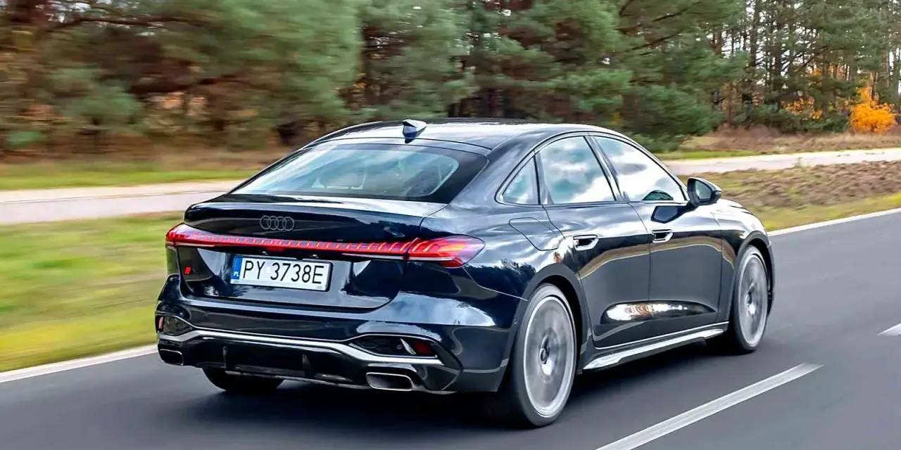 Ciemny Audi A4 B10 pędzi po drodze, otoczony jesiennym lasem.
