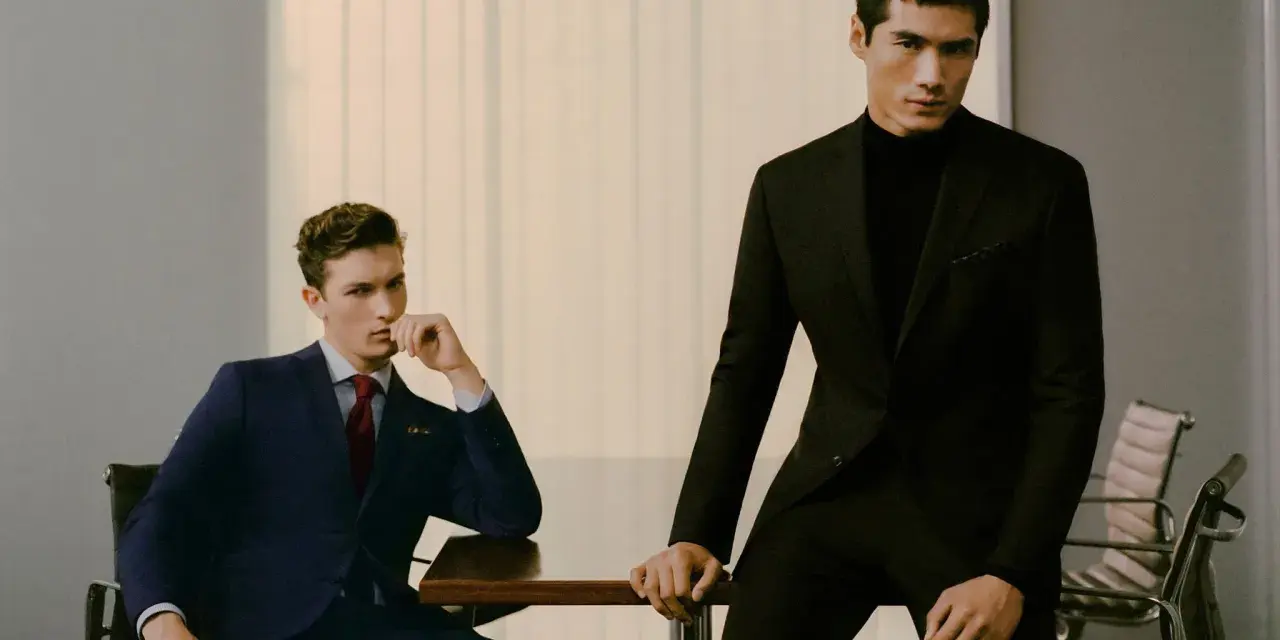 Dos hombres con trajes elegantes, uno azul y otro negro, demuestran el estilo business casual en una oficina moderna.