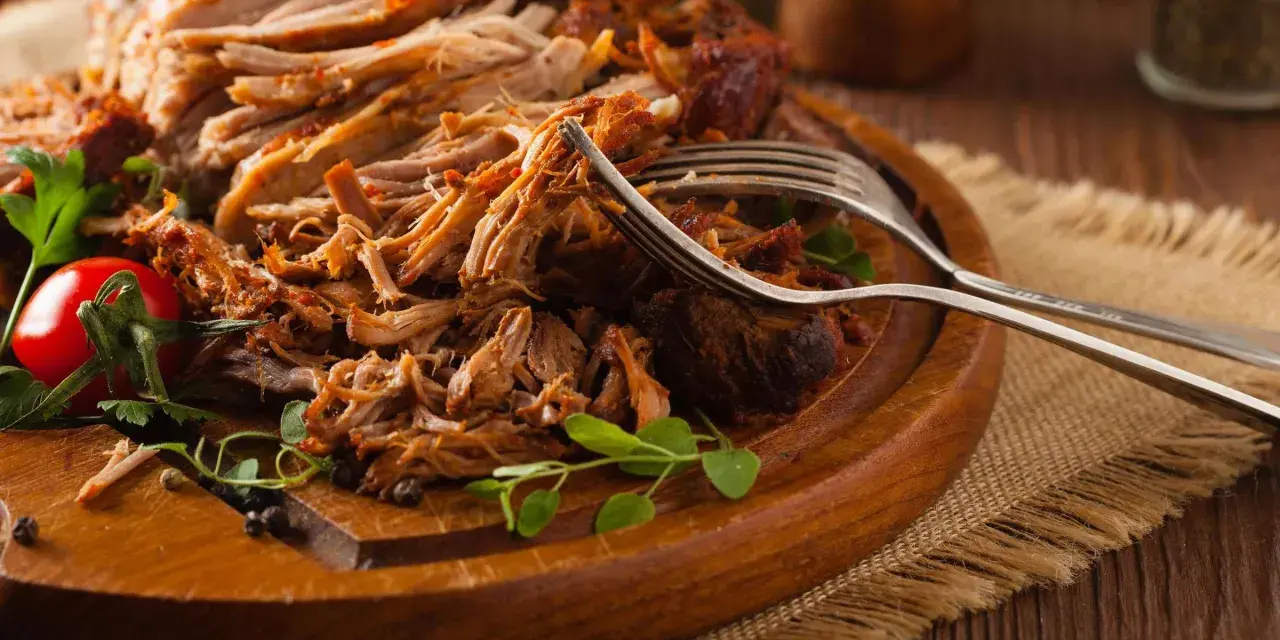 Saftiges Pulled Pork, perfekt zubereitet mit einem aromatischen pulled pork rub, liegt auf einem Holzbrett. Gabeln deuten auf den Genuss hin.