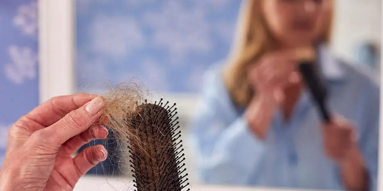 Frauen mit Haarausfall halten eine Bürste mit vielen Haaren. Im Spiegel sieht man eine Frau, die sich die Haare kämmt.