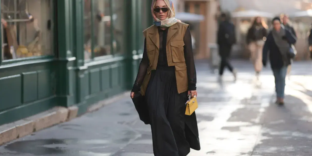 Mujer con chaleco negro corto, falda larga negra y bolso amarillo.