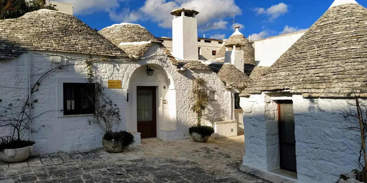 Urokliwe domki trulli z kamiennymi dachami, malownicze uliczki i błękitne niebo.