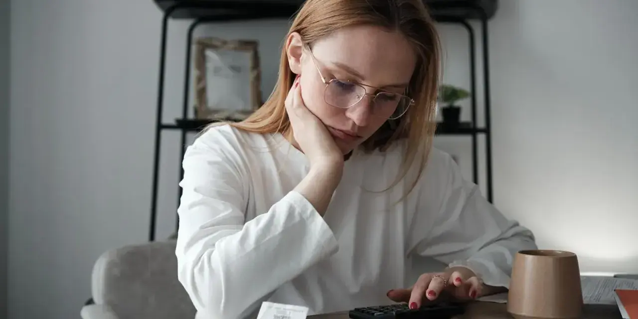Zmartwiona kobieta z okularami liczy na kalkulatorze, szukając informacji, jak sprawdzić zadłużenie alimentacyjne.