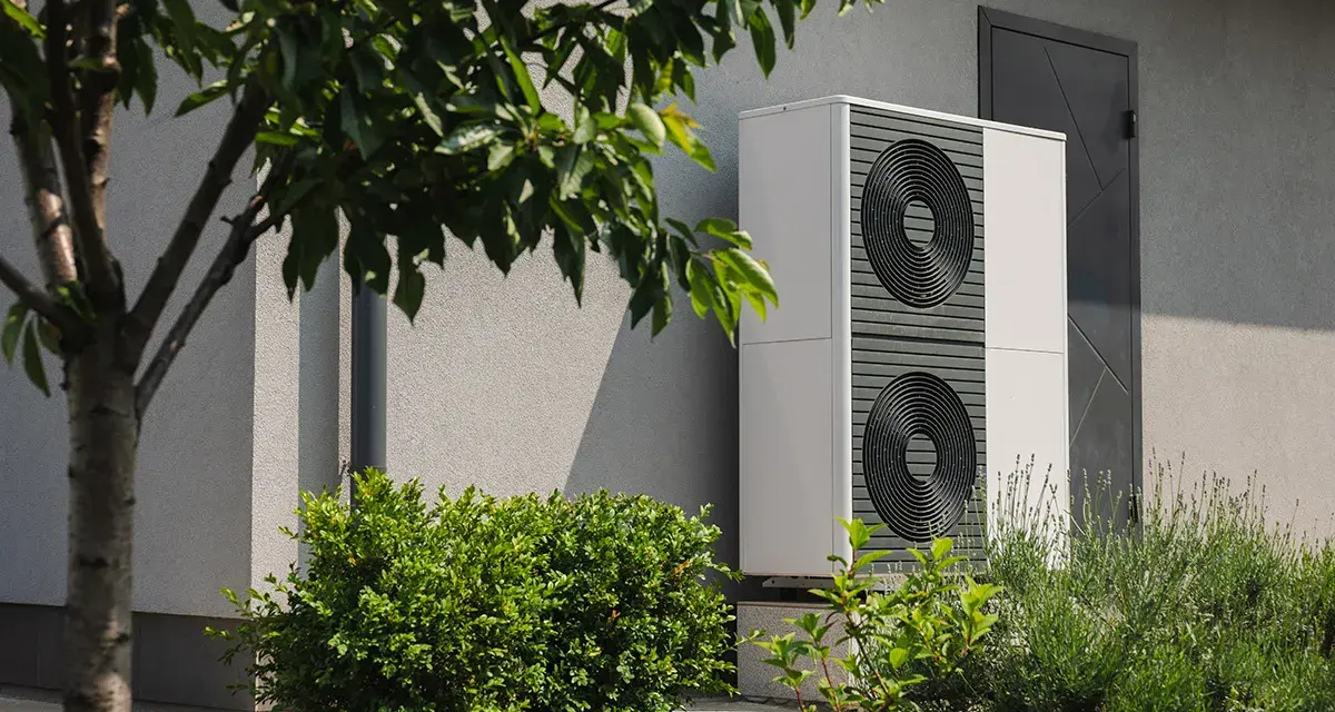 Nowoczesna pompa ciepła 3 5 kw, dyskretnie umieszczona przy ścianie domu, otoczona zielenią, zapewnia ekologiczne ogrzewanie.