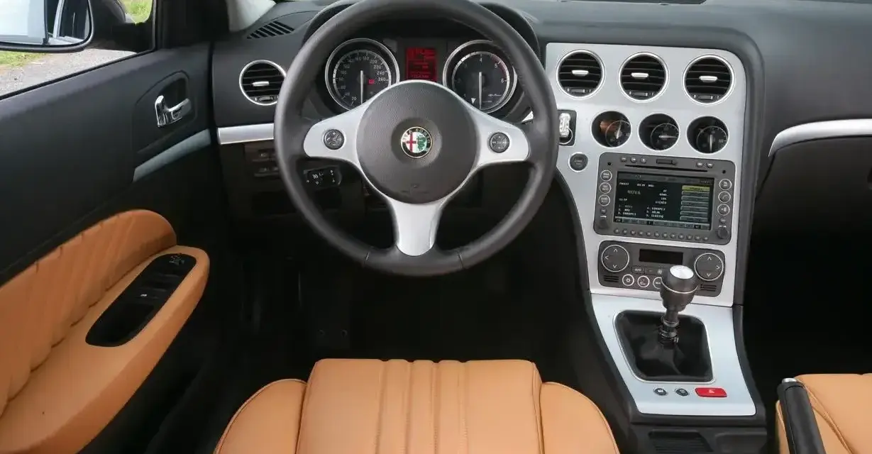 Wnętrze Alfa Romeo 159 1.9 JTD z beżową skórzaną tapicerką, kierownicą i konsolą środkową.