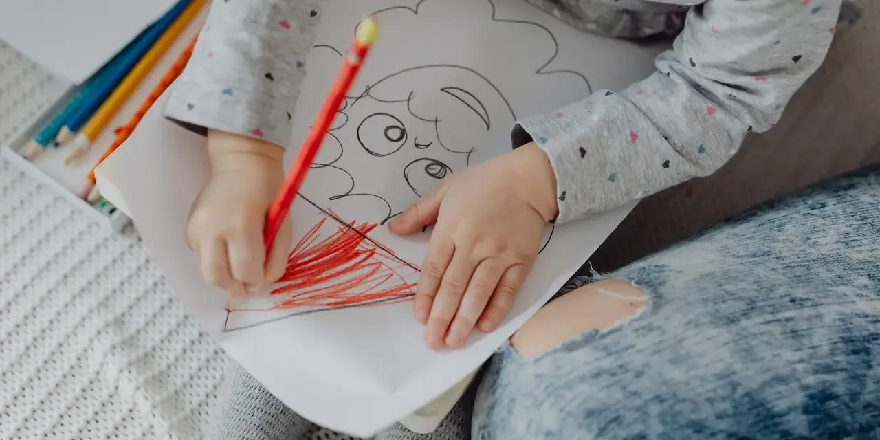 Mały rysunek dziecka z kredkami. Dziecko koloruje czerwoną kredką.