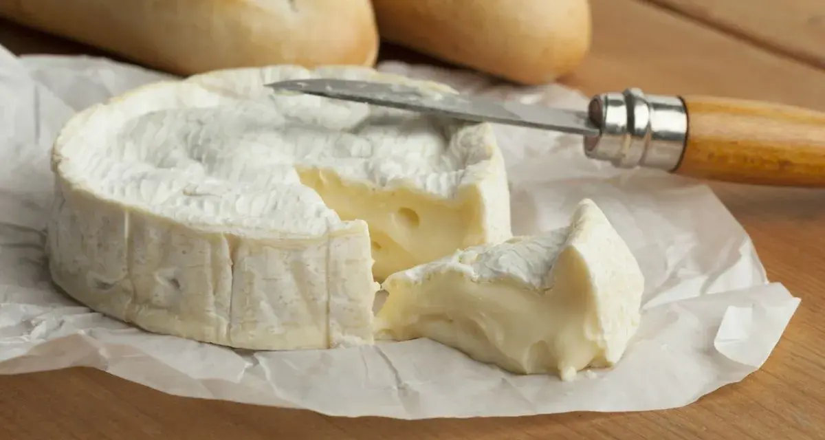 Un trozo cremoso de le camembert, con una rebanada cortada y lista para untar en pan crujiente.