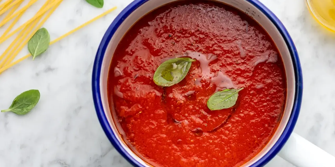 Sugo con pomodorini freschi, basilico e spaghetti crudi su marmo.