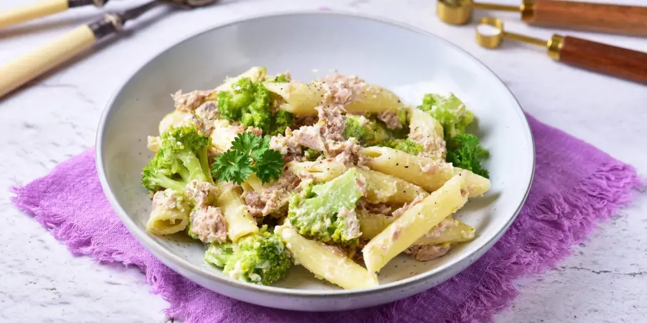 Penne z tuńczykiem i brokułami w kremowym sosie śmietanowo-serowym, udekorowane natką pietruszki.