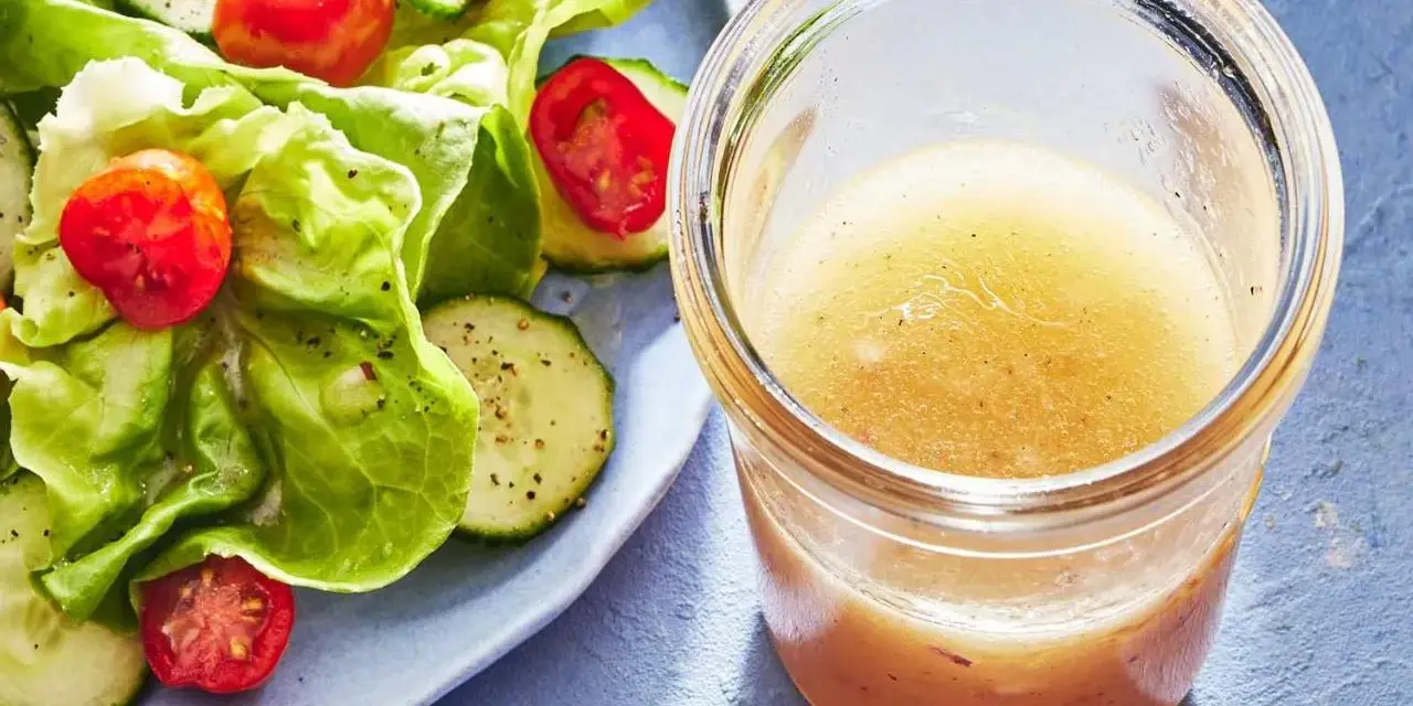 En burk med gyllene dressing till sallad står bredvid en fräsch sallad med sallad, gurka och tomater.