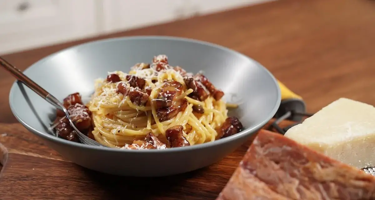 Miseczka spaghetti carbonara z boczkiem i parmezanem, obok kawałki sera i boczku.