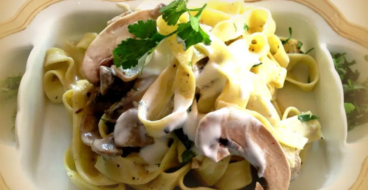 Pyszne tagliatelle z grzybami w kremowym sosie, udekorowane natką pietruszki.