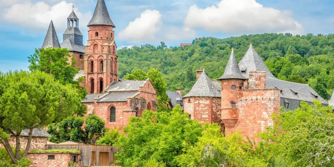 Magnifique ensemble de bâtiments en pierre rouge, dont une église romane et des tours, au milieu d'une végétation luxuriante. Idéal pour découvrir que faire autour de Rocamadour.