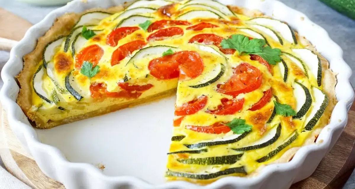 Eine köstliche Zucchini-Quiche mit Tomaten und frischer Petersilie, in einer weißen Quicheform serviert.