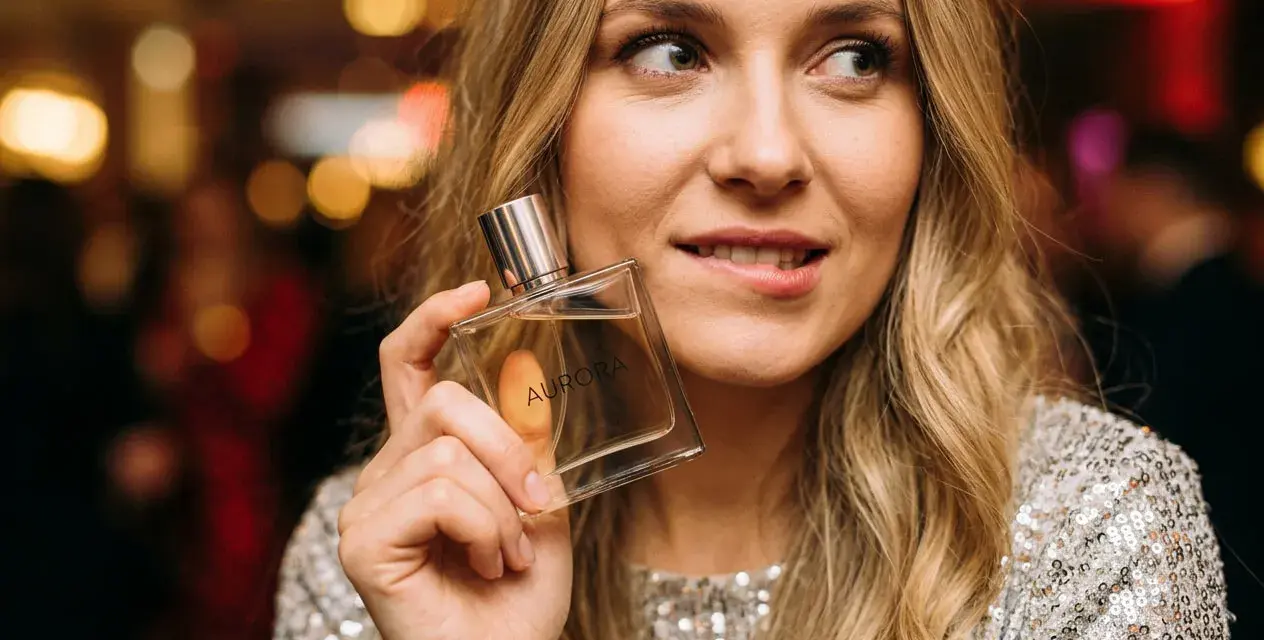 Kobieta z flakonem perfum "Aurora" zastanawia się, czy ma w sobie to coś, co przyciąga mężczyzn.