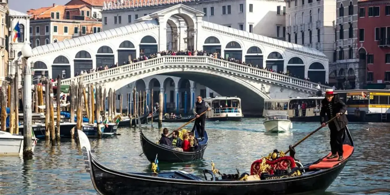 La gondola veneziana scivola sull'acqua, con il Ponte di Rialto sullo sfondo, un'icona di Venezia.