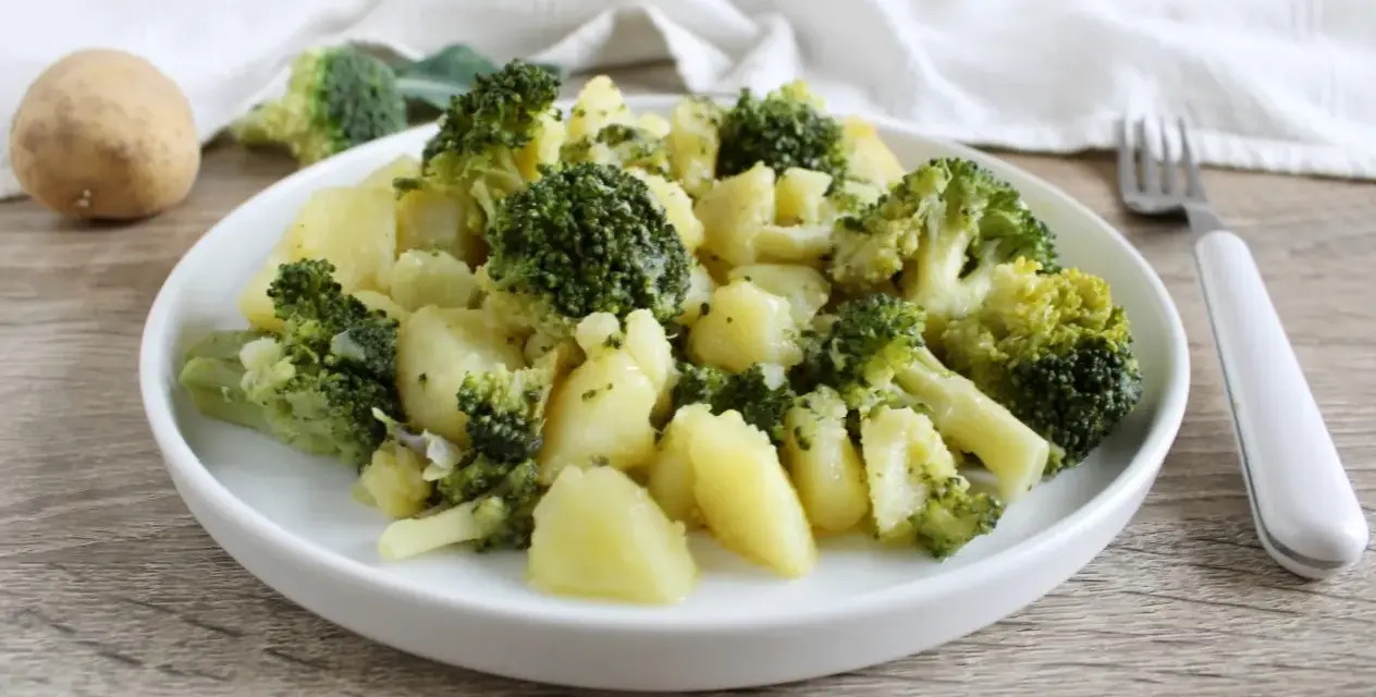 Un plato de brócoli con patatas, sencillo y saludable. Una patata entera y trozos de brócoli reposan cerca.