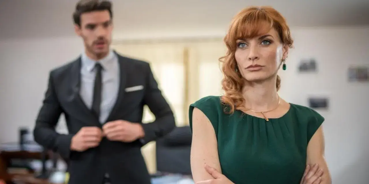 Donna con sguardo preoccupato, mentre un collega in primo piano si sistema la giacca, come se volesse metterla in cattiva luce.