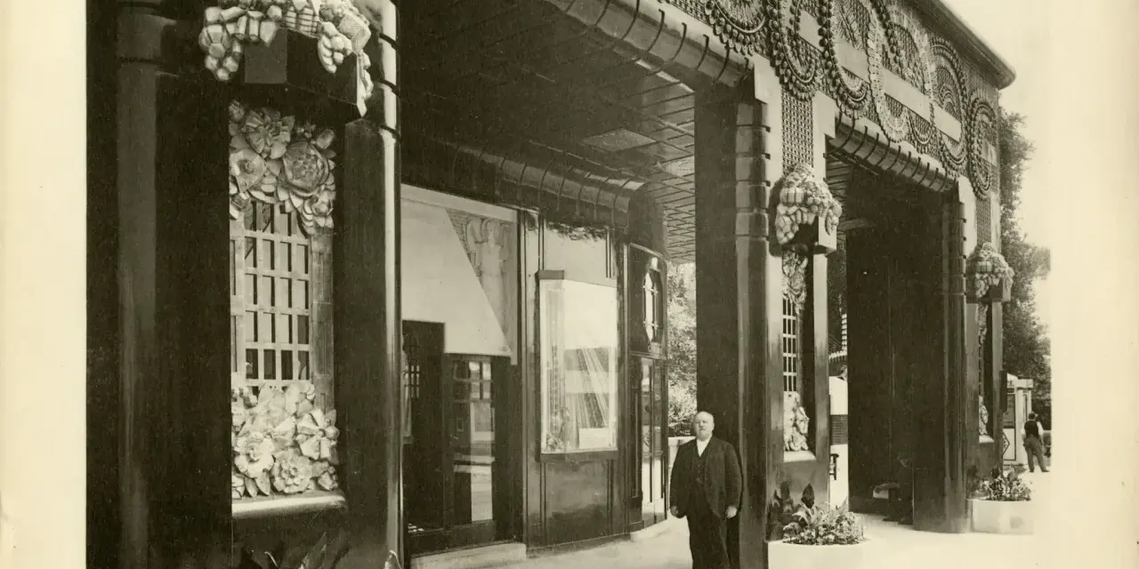 Façade de galerie de boutiques, style art déco, avec ornements floraux et motifs circulaires. Un homme en costume se tient sur le trottoir.
