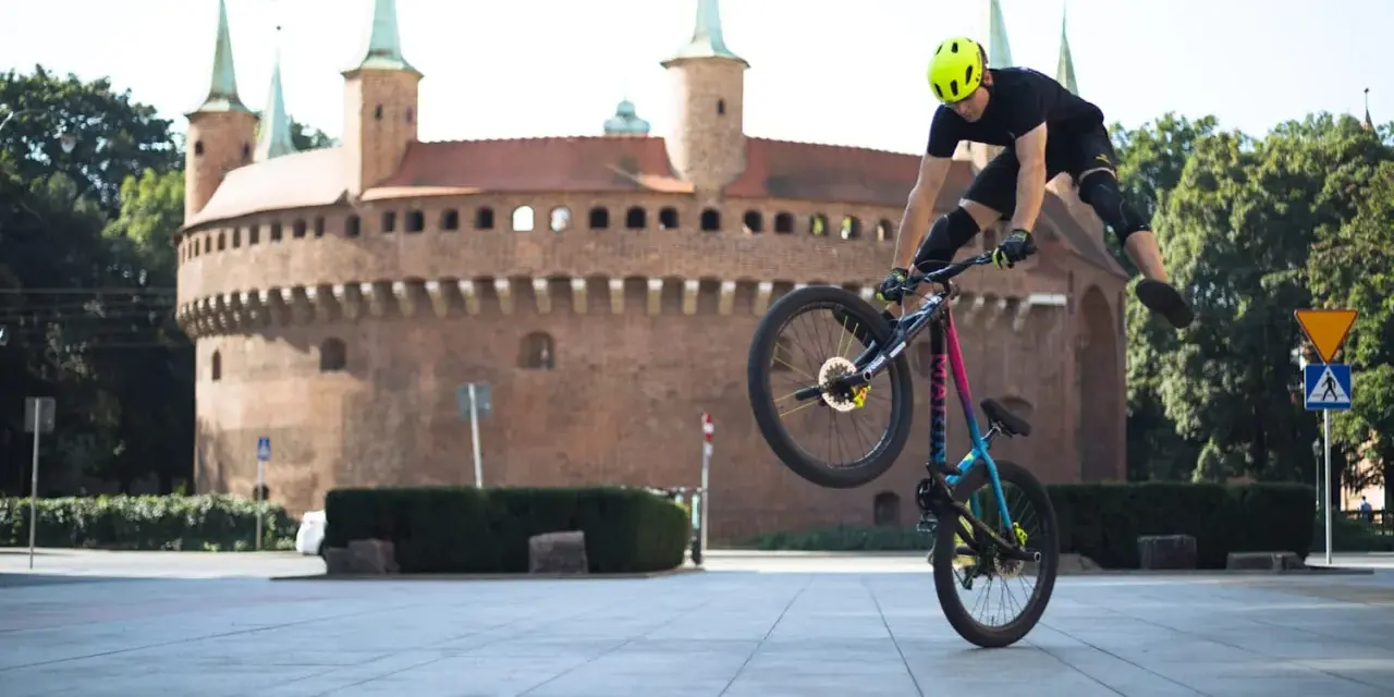 Kraków rowerem: kaskader na rowerze wykonuje akrobację przed Barbakanem.