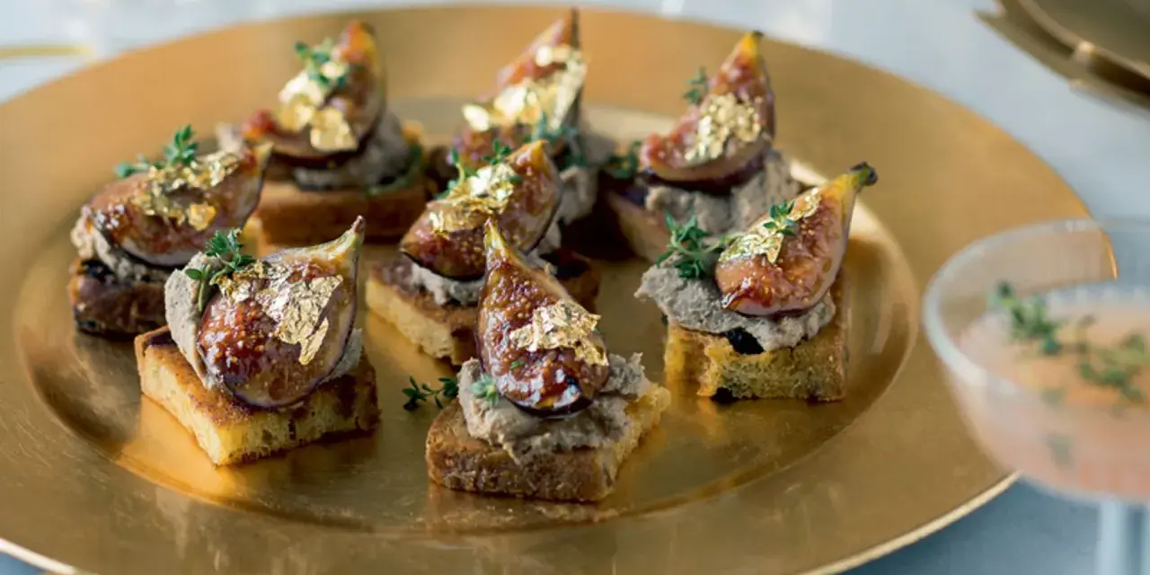 Deliciosos higos con foie sobre tostadas, adornados con pan de oro y tomillo, servidos en una bandeja dorada.