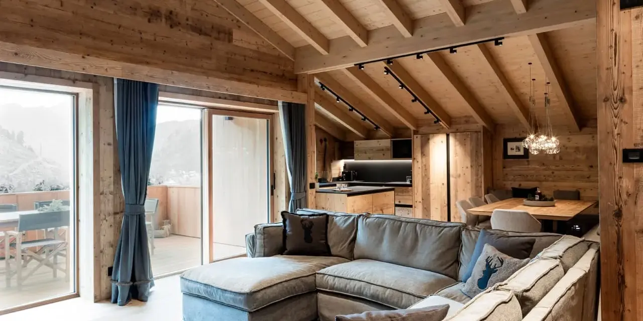Cozy mountain chalet living room with sectional sofa, wooden beams, and large windows.
