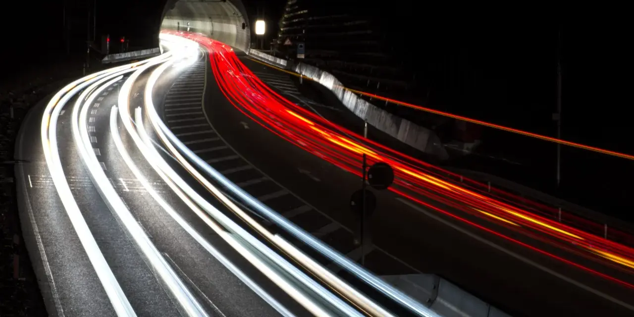Voiture traversant un tunnel la nuit, capturant les traînées lumineuses des phares et des feux arrière grâce à des photos pose longue.