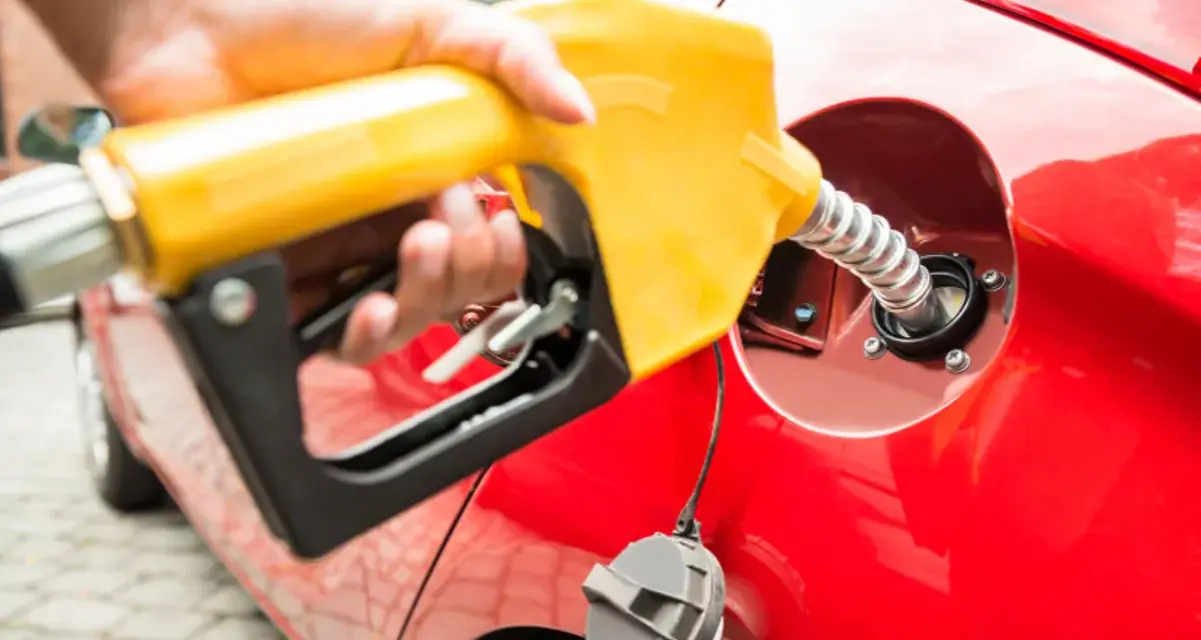 En hand håller en gul pump för att tanka en röd bil. Undrar du vad kostar diesel i Norge?