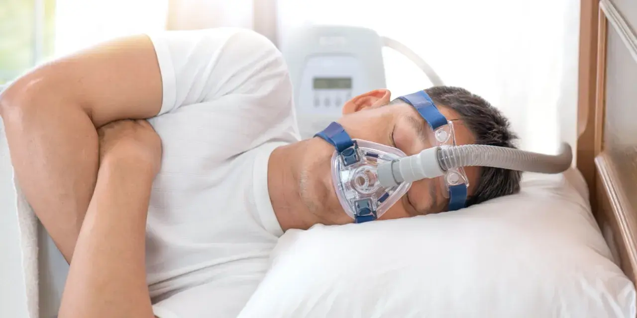 Mężczyzna śpi z maską CPAP, która pomaga mu oddychać podczas bezdechu sennego.