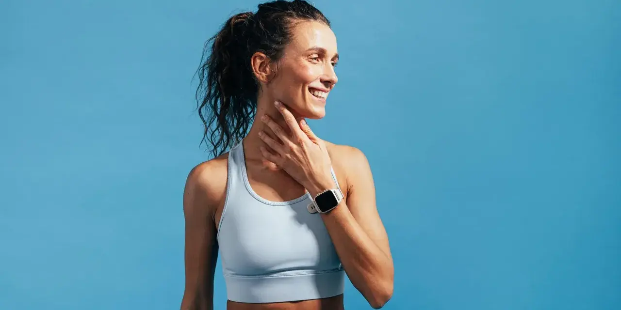Donna sorridente con orologio sportivo, tocca il collo. Nonostante la sensazione di correre con la febbre, il suo sguardo è positivo.