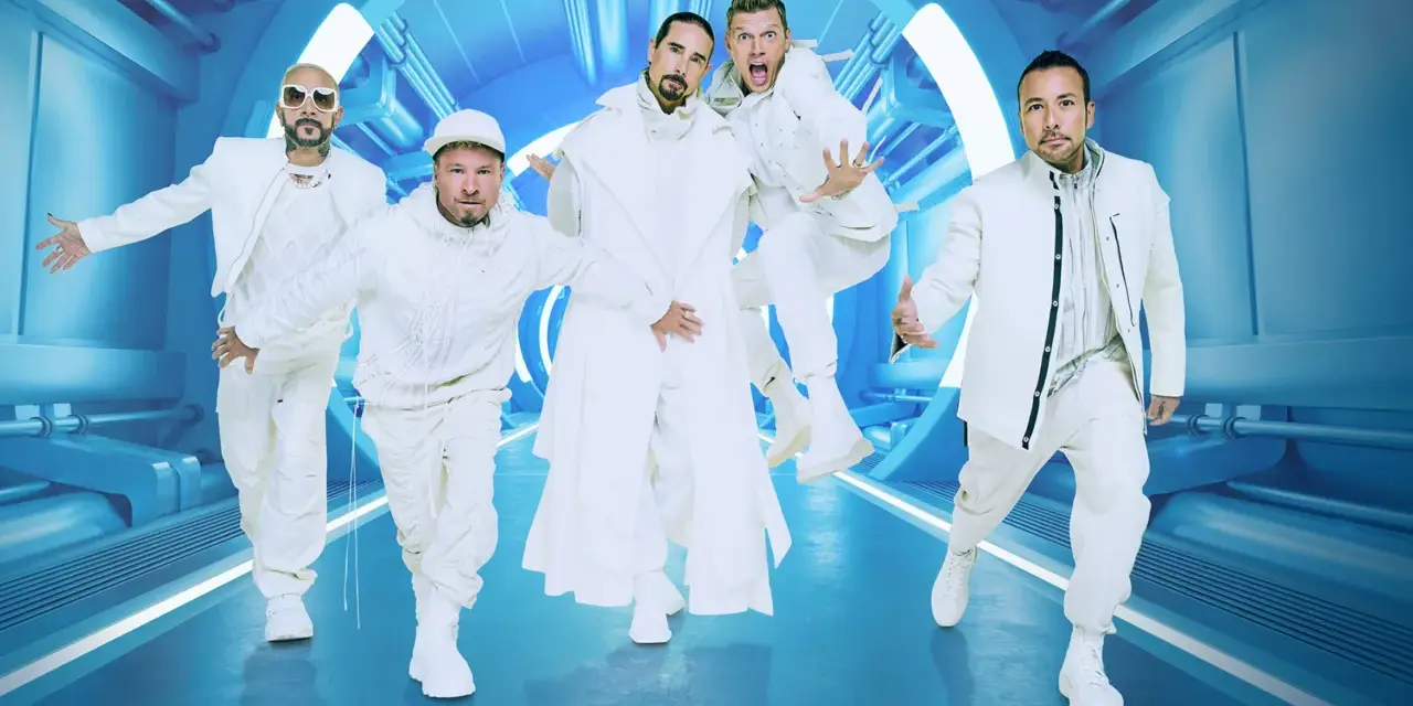 Backstreet Boys w białych strojach, gotowi na koncert. Ich energia jest zaraźliwa, a futurystyczna scenografia podkreśla ich styl.