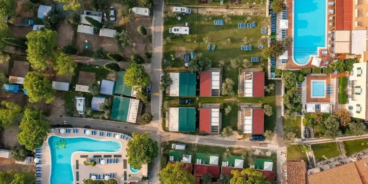 Widok z lotu ptaka na camping Toscolano: domki, baseny, przyczepy kempingowe i zielone tereny.