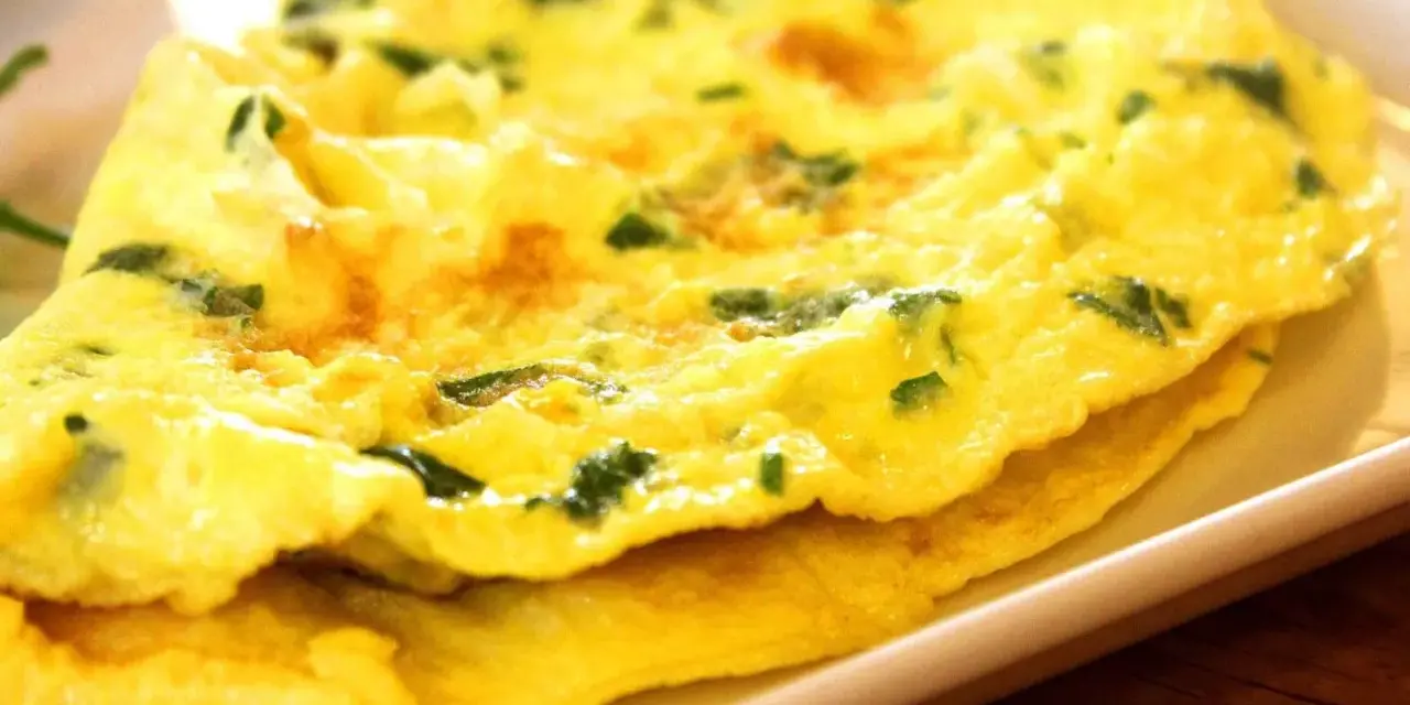 Złożony omlet z zielonymi ziołami na białym talerzu.
