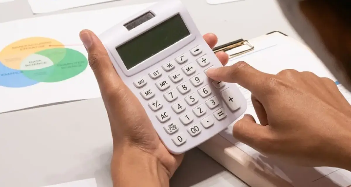 Persona calculando con calculadora blanca, rodeada de gráficos de tendencias y diagramas de Venn, analizando datos para gestionar masas patrimoniales.