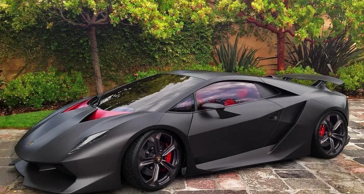 Matowy czarny Lamborghini Sesto Elemento z czerwonymi akcentami i wnętrzem, zaparkowany na brukowanej ścieżce wśród zieleni.