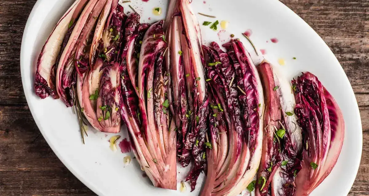 Radicchio al forno, tagliato a spicchi e condito con erbe aromatiche, servito su un piatto bianco.