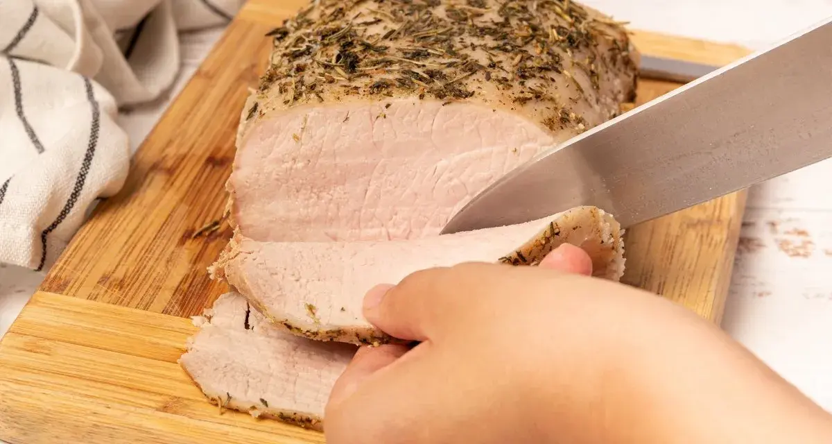 Un jugoso lomo a la sal, cubierto de hierbas, se corta en rodajas tiernas sobre una tabla de madera.