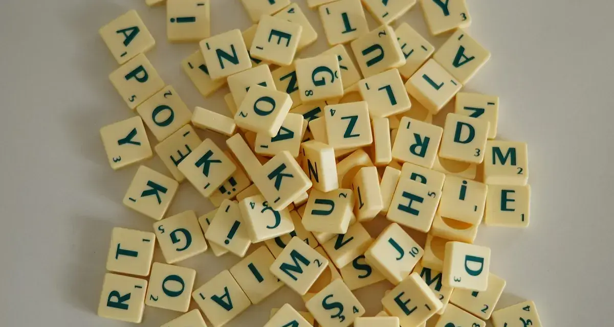 Fichas de letras de un juego de mesa, como las del Scrabble, dispersas. Cada ficha tiene una letra y un número. Un ejemplo visual de la diferencia entre lengua e idioma.