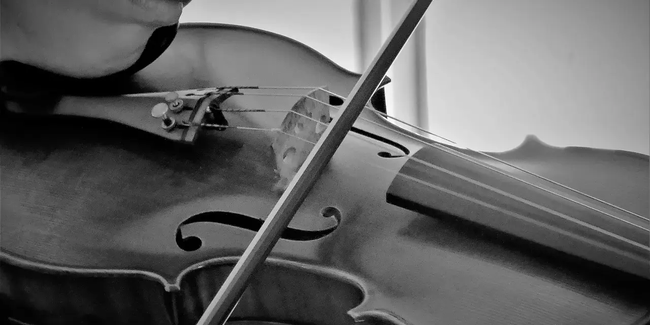 Nahaufnahme einer Person, die eine Geige spielt. Der Bogen streicht über die Saiten und erzeugt die Klänge bester klassischer Musik.