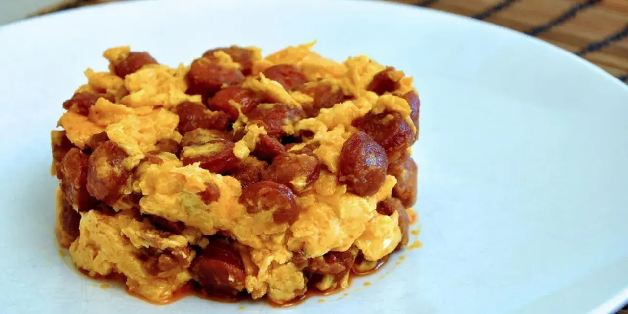 Deliciosa porción de duelos y quebrantos receta, con huevo revuelto y trozos de chorizo, servida en plato blanco.