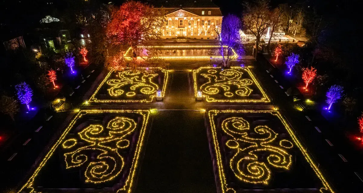 Magische Lichtershow im Tierpark Berlin: Verzauberte Gärten mit leuchtenden Mustern und farbig beleuchteten Bäumen vor einem prachtvollen Gebäude.