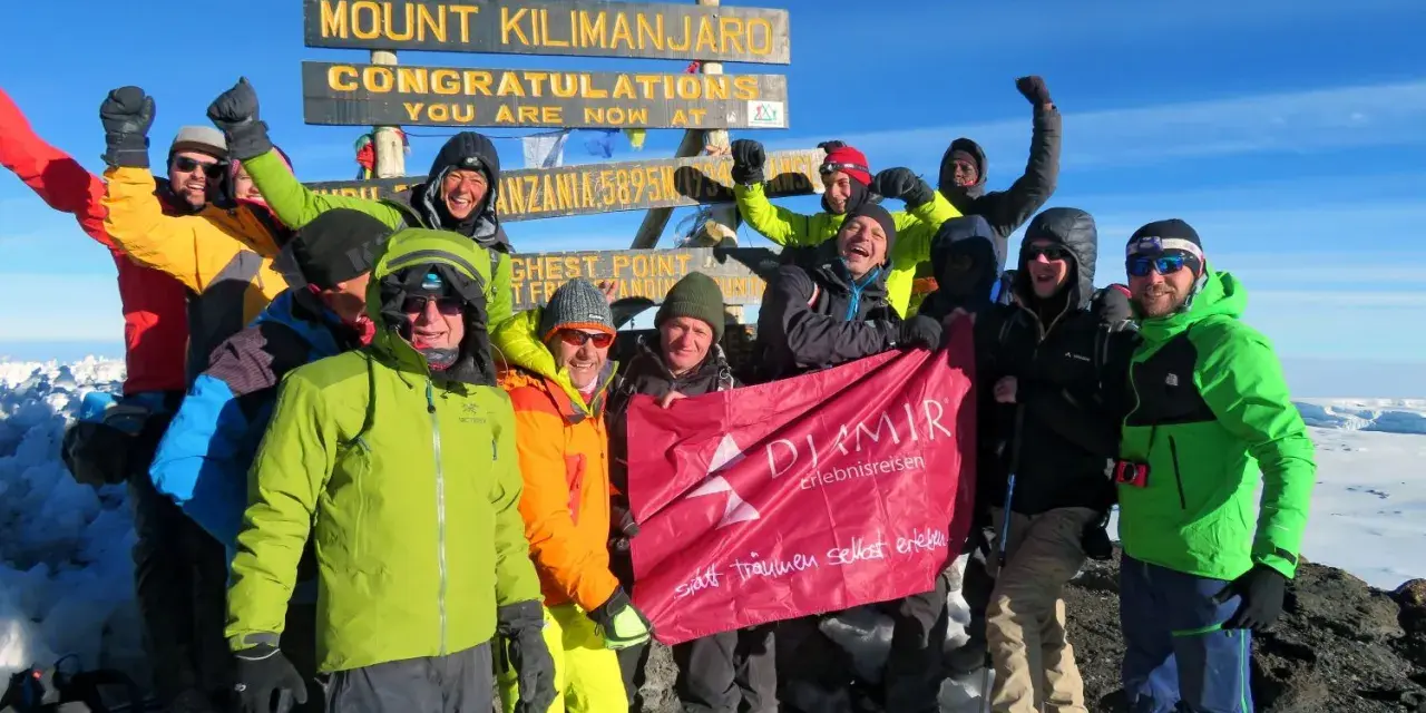Glückliche Gruppe feiert auf dem Gipfel des Kilimandscharo. Sie haben den Gipfel erreicht und halten ein Banner hoch. Ein unvergessliches Erlebnis, den Kilimandscharo zu besteigen!