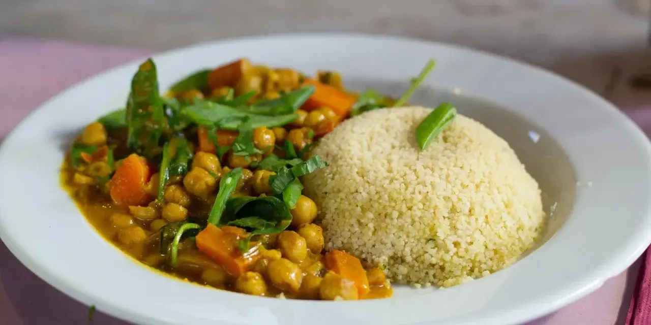 Un plato de cuscus con verduras, garbanzos y zanahoria en una salsa dorada, decorado con hojas verdes.